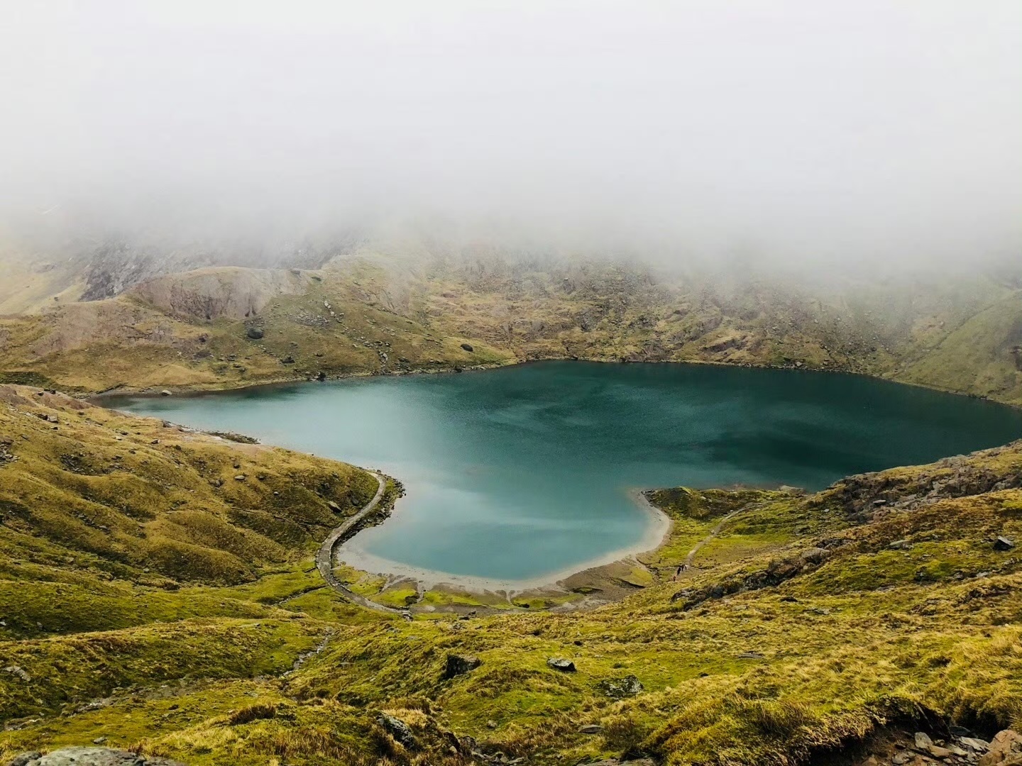 A misty mountain lake surrounded by green slopes